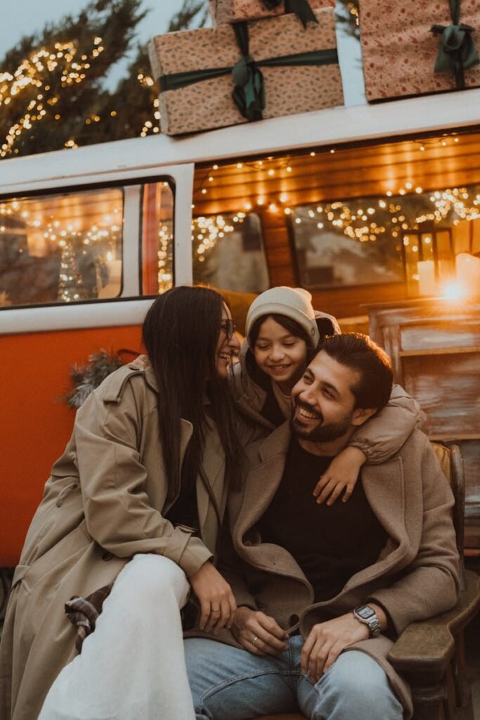 A family enjoys a warm, joyful moment outside a decorated camper van with string lights.